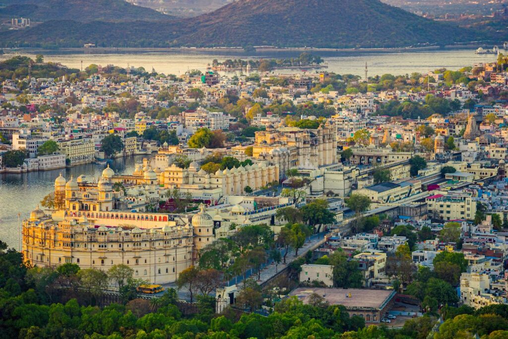 Aerial view of the historic Udaipur City Palace and surrounding cityscape against a tranquil lake backdrop.