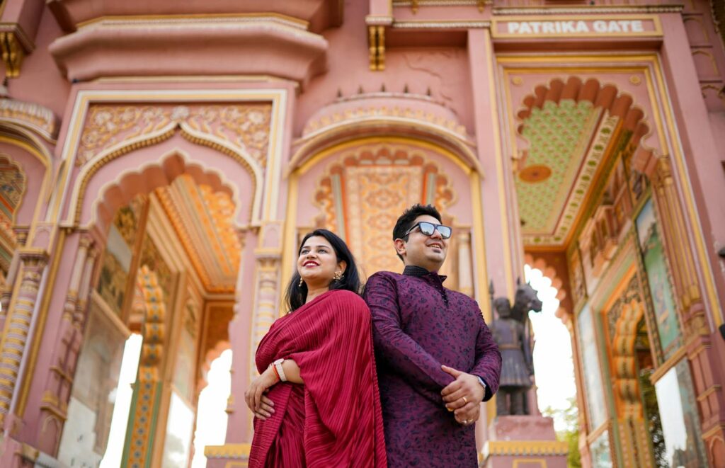 Indian couple in traditional clothing smiling at Patrika Gate, Jaipur, creating a vibrant cultural image.